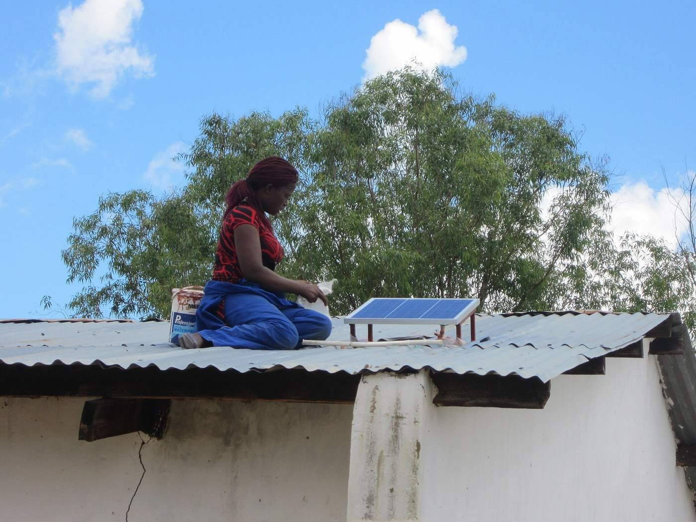Woman solar technician mounting a panel on a roof, Malawi